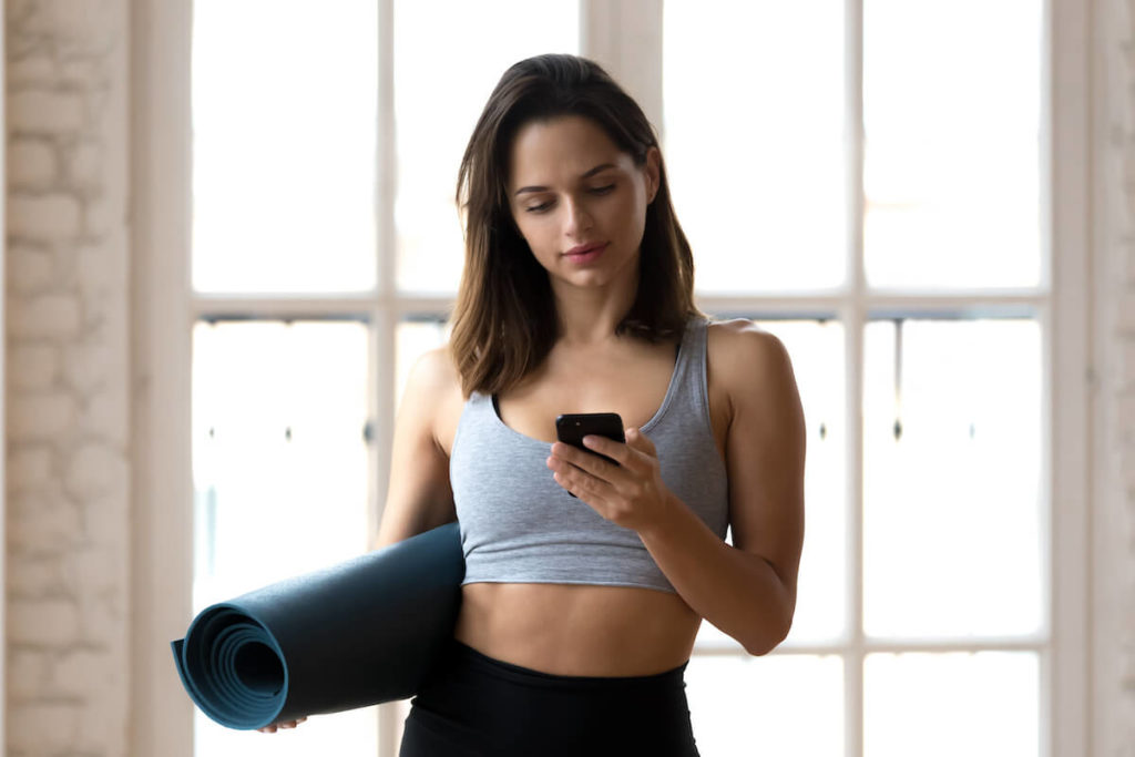 Yoga advertising: woman carrying a yoga mat while using her phone