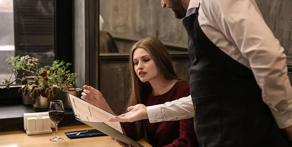 Pricing strategies: waiter in restaurant showing customer a menu