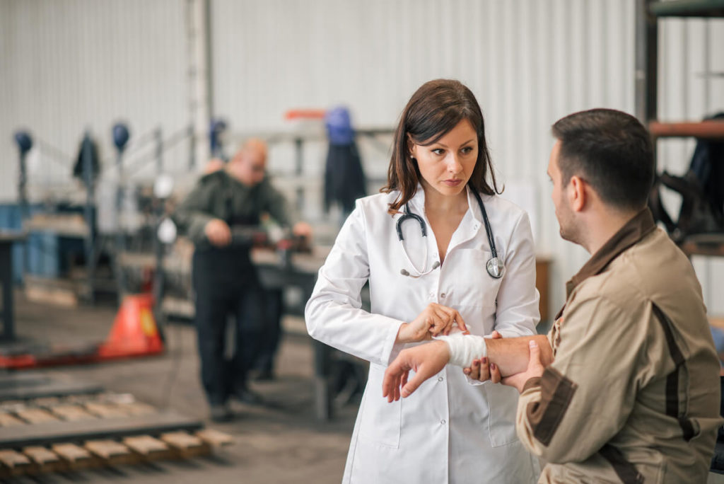 Types of business insurance: doctor bandaging the wrist of an injured worker