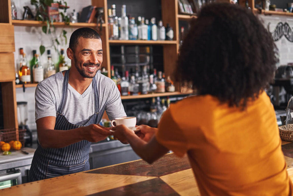 Return customers: waiter handing a cup of coffee to a customer