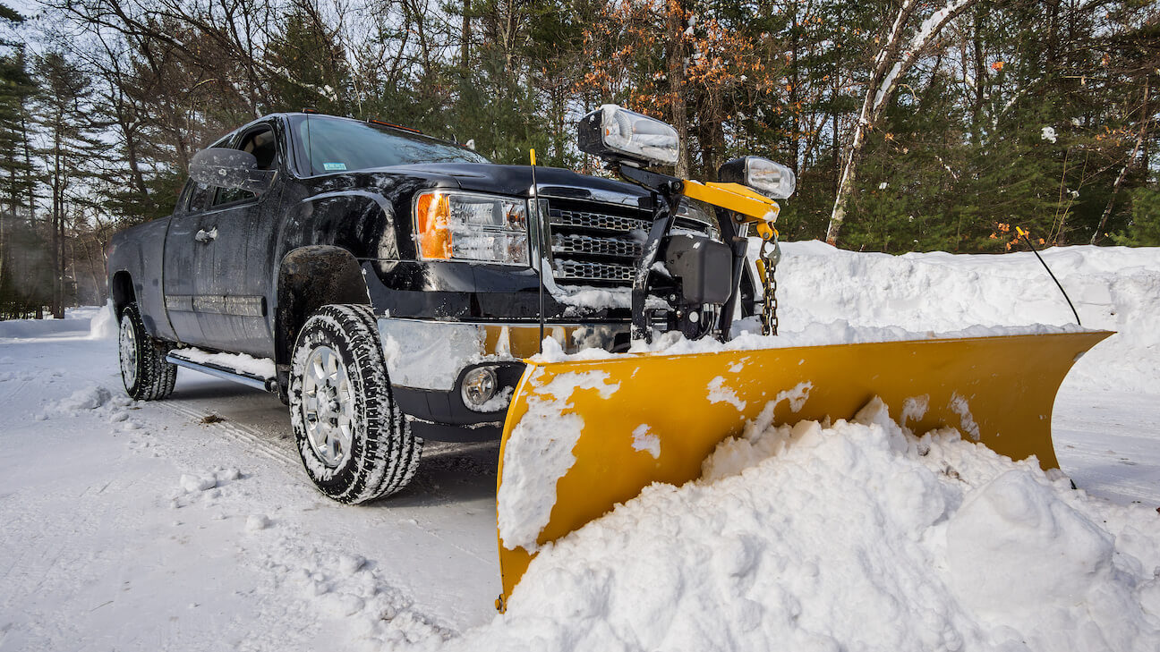 Snow removal leads: pickup truck with a snowplow clearing a road