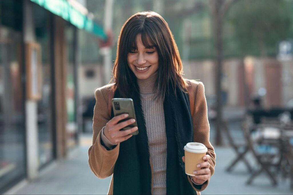 Woman using her phone while holding a cup of coffee