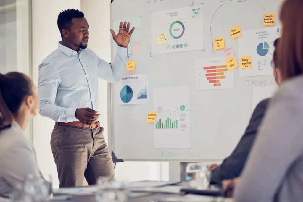 Man at a whiteboard presenting marketing budget metrics to a team of marketers