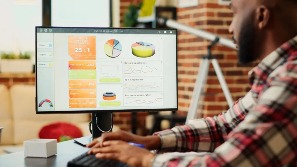 Man looking at a desktop computer screen featuring numbers and graphs