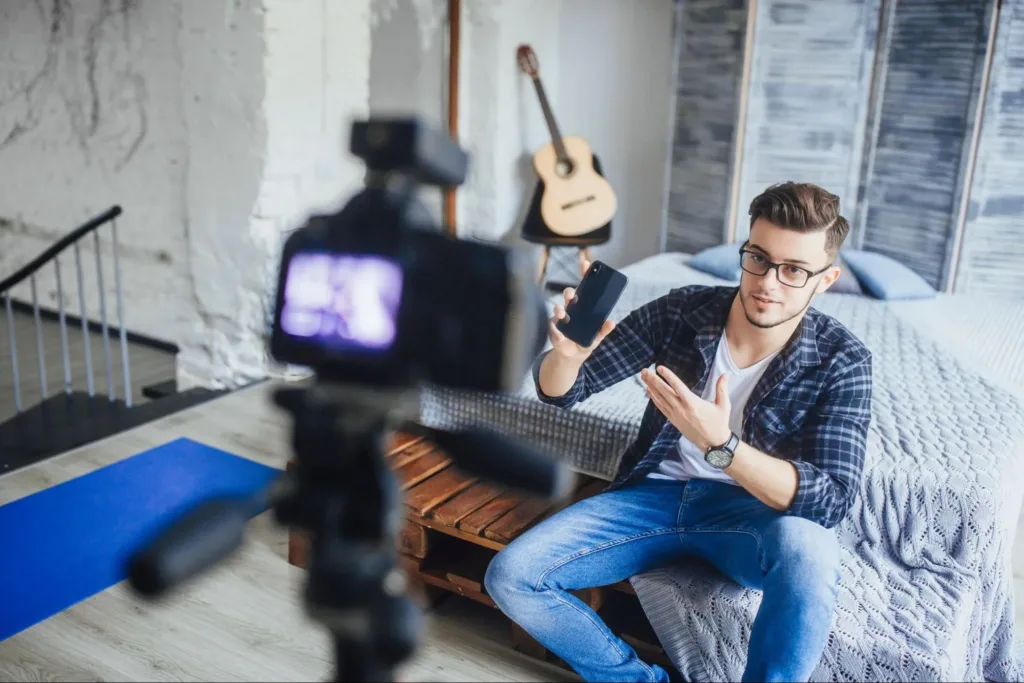 Man in his room with a guitar and a phone while filming himself for influencer marketing purposes