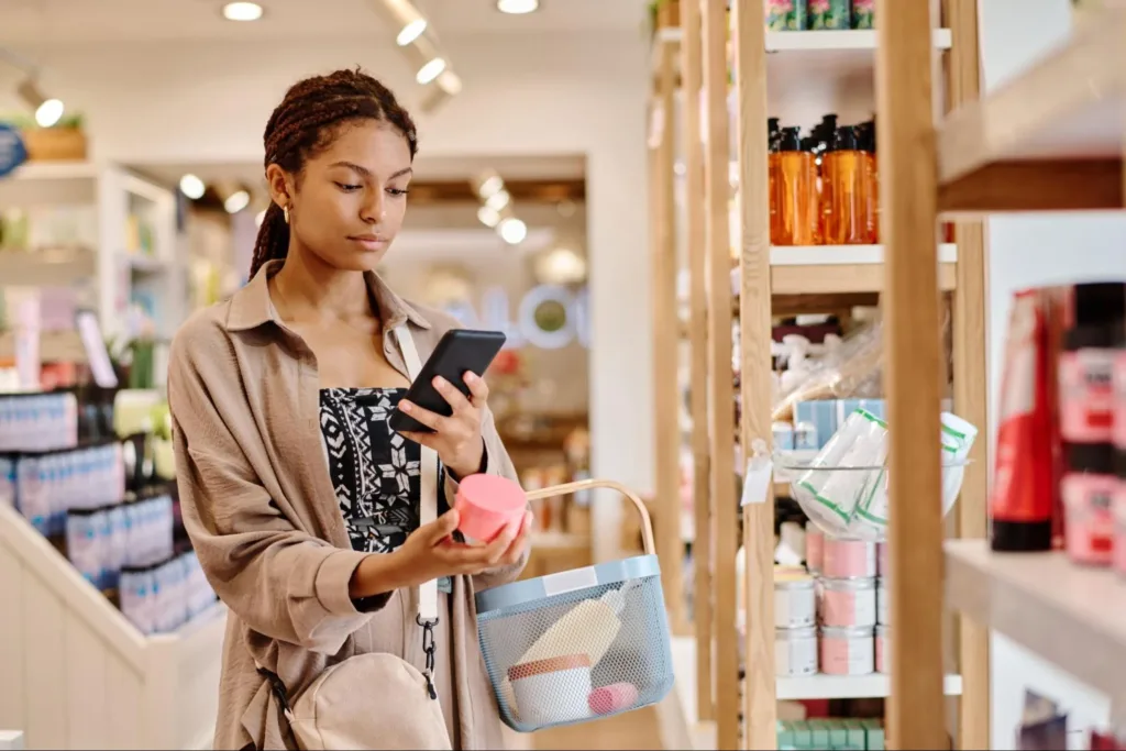 Woman shopping in a store while looking at her phone and putting an item in her basket