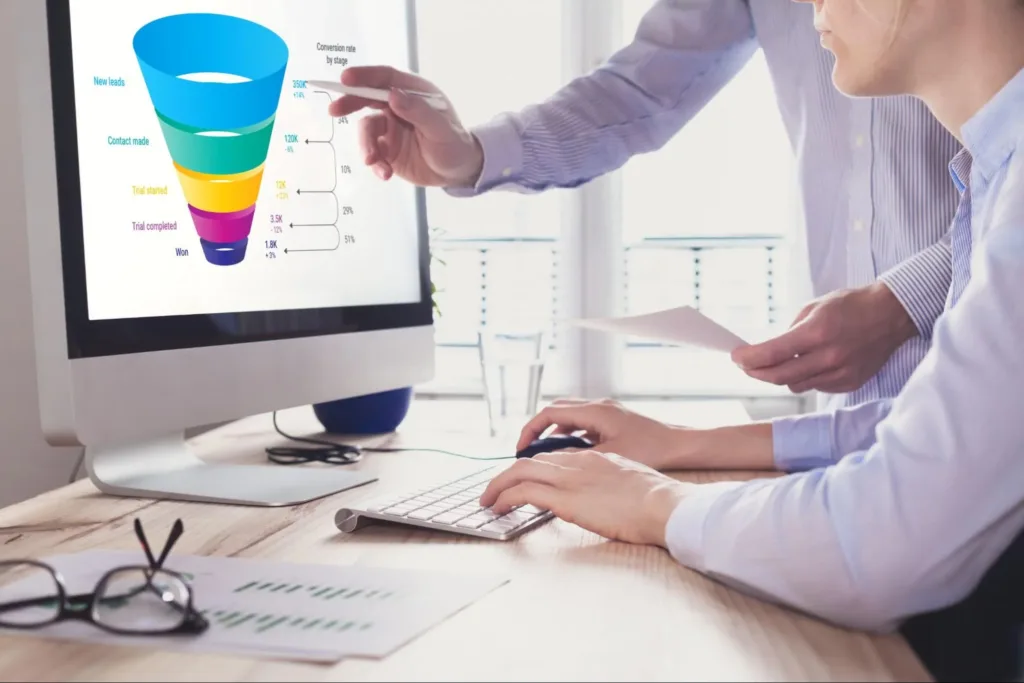 Two professionals at a desk looking at a computer screen featuring a funnel representing different stages of the marketing funnel