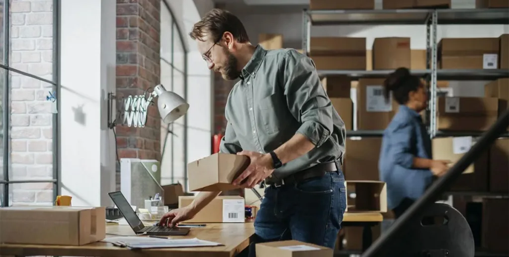 Small business owner using laptop while holding a small box