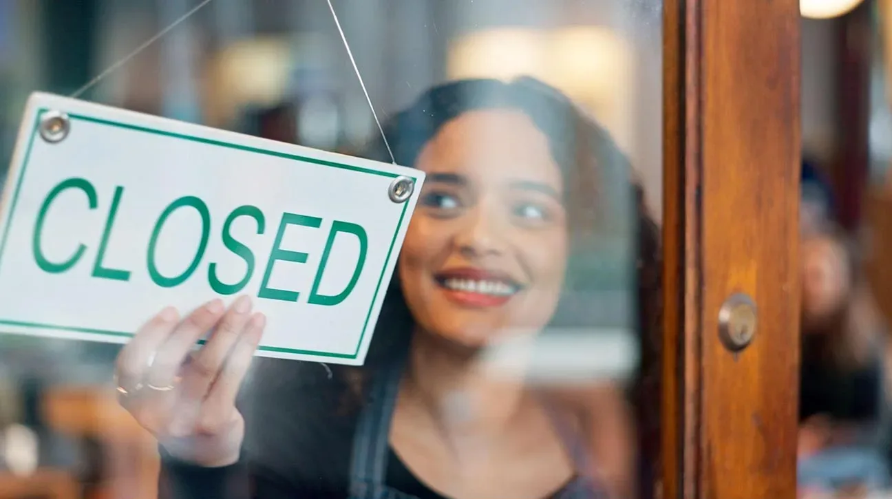 Businesswoman hanging a closed shop sign at window