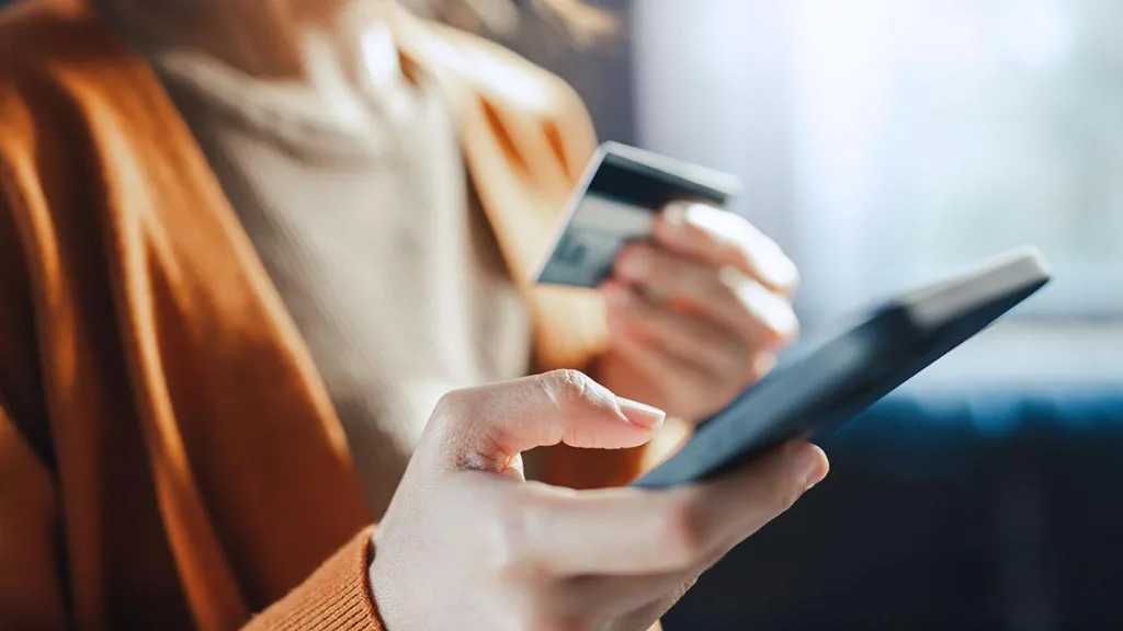 Woman holding a credit card in one hand and a smartphone in the other to make an online purchase