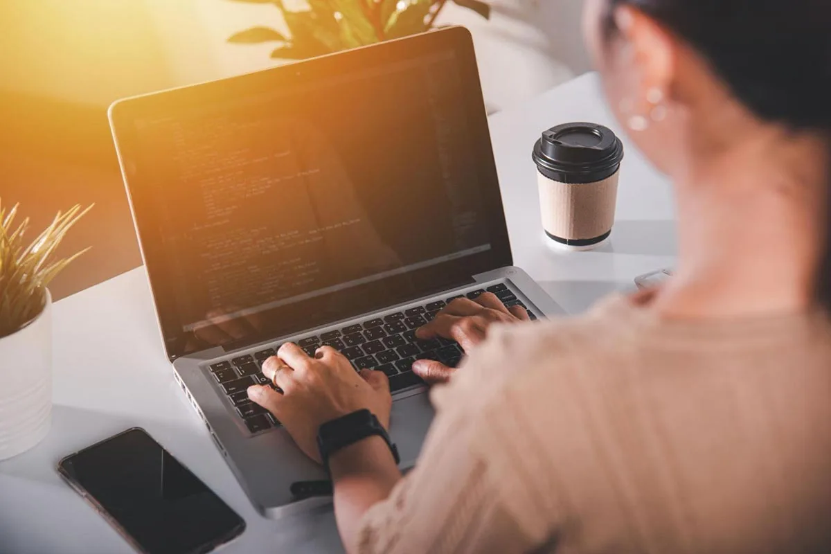 A small business owner working on her laptop with a cup of coffee beside her