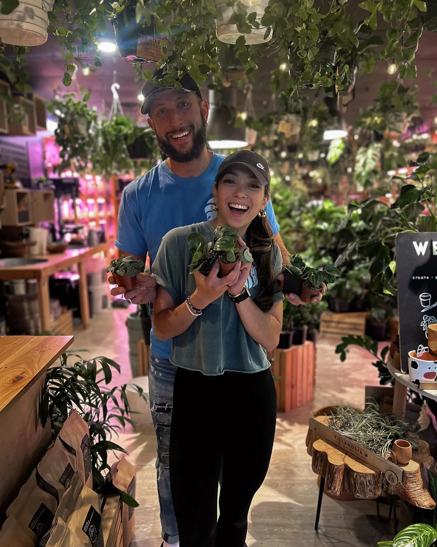 Owner Sam Shaw and husband Matt smiling inside the store holding potted plants