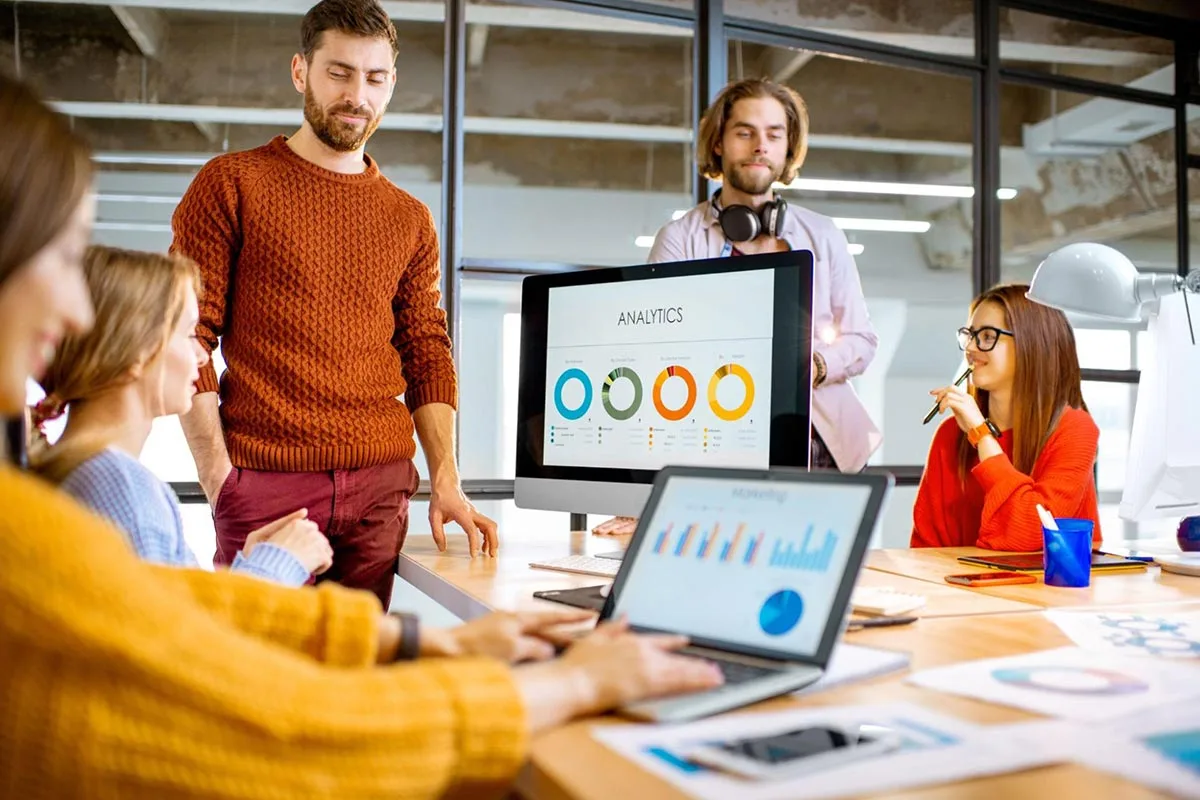 Team of marketing managers reviewing analytics on a laptop in a modern office setting