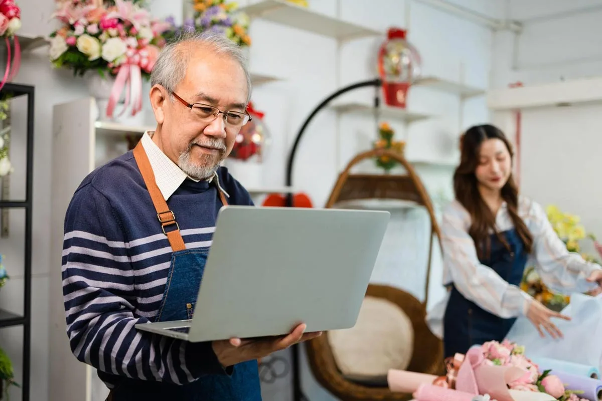 A family florist holding a laptop while standing in their flower shop