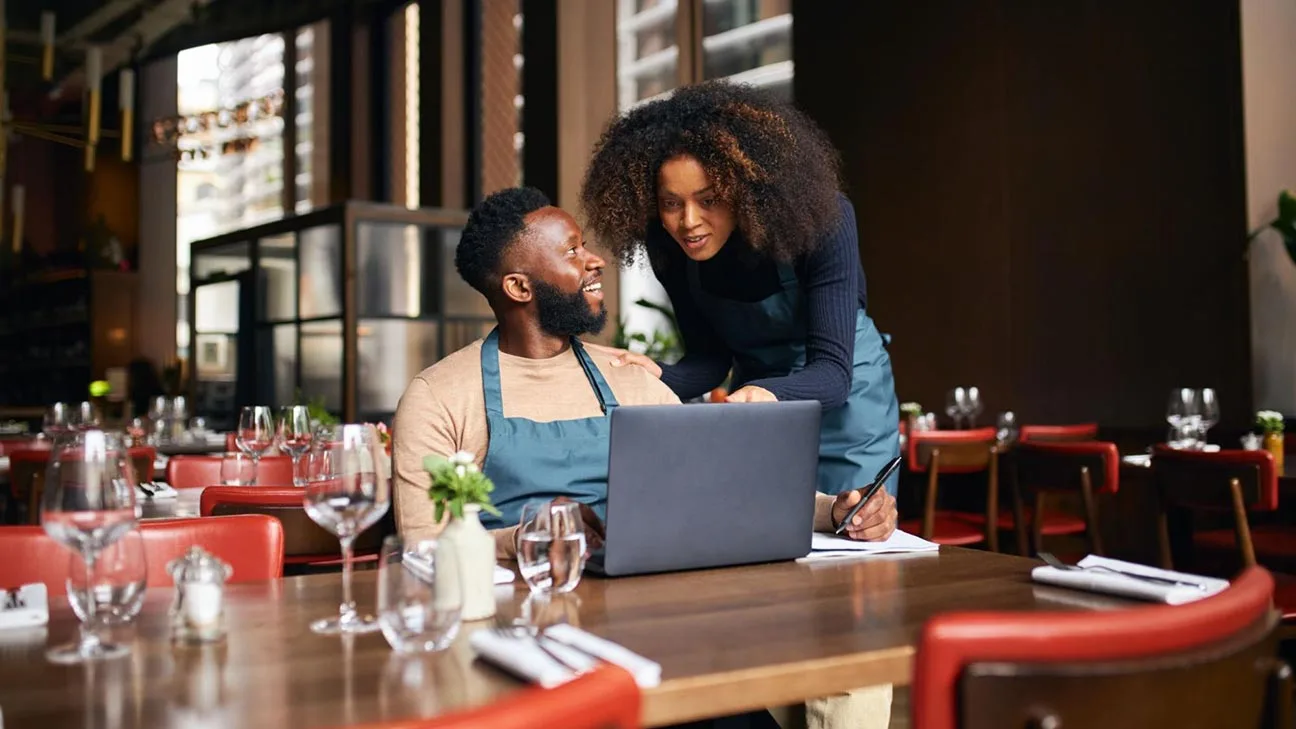 Two restaurant owners collaborating in their restaurant to create effective lead generation ads on a laptop