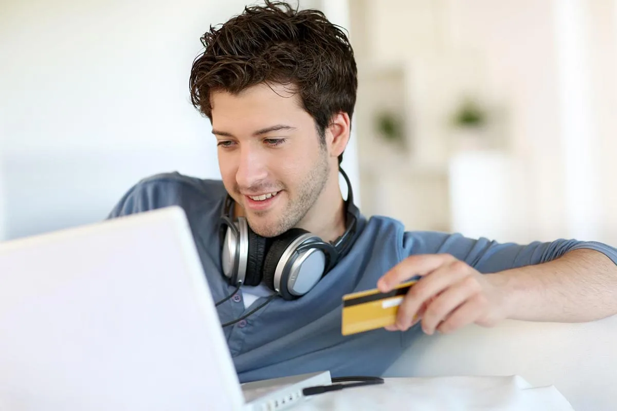 Young man sitting in his living room using a bank card to make a payment on his phone