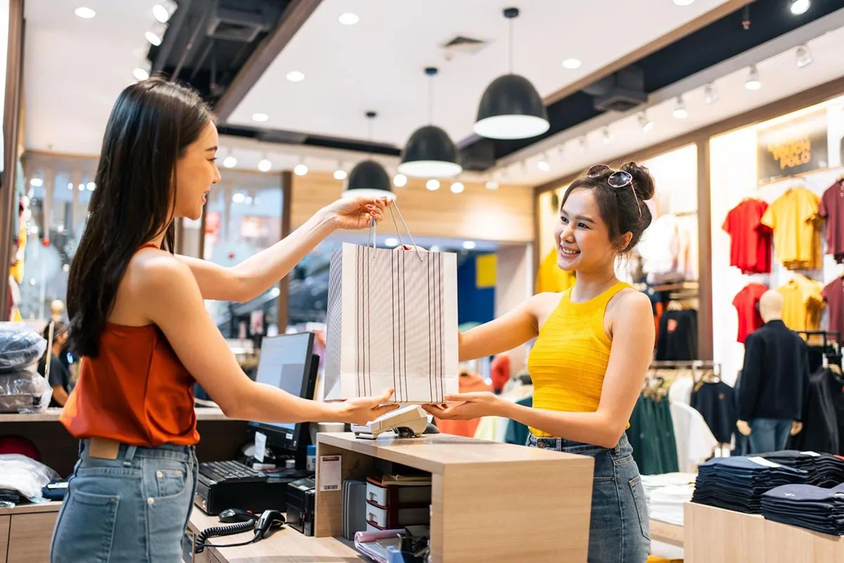 Brand lift: A store owner handing over a shopping bag to a customer, smiling as they complete the transaction.