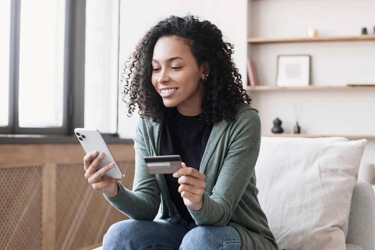 Omnichannel marketing: a woman sitting on a chair in her home, using a smartphone to make a card payment online