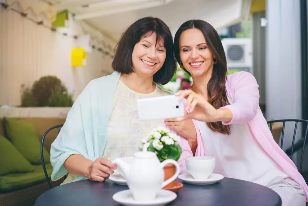 Mother and daughter smiling while taking a photo booth selfie together at a restaurant.