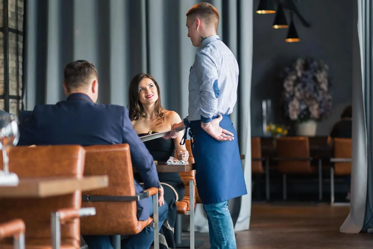 A restaurant server talking to a couple seated at a table during their dining experience.