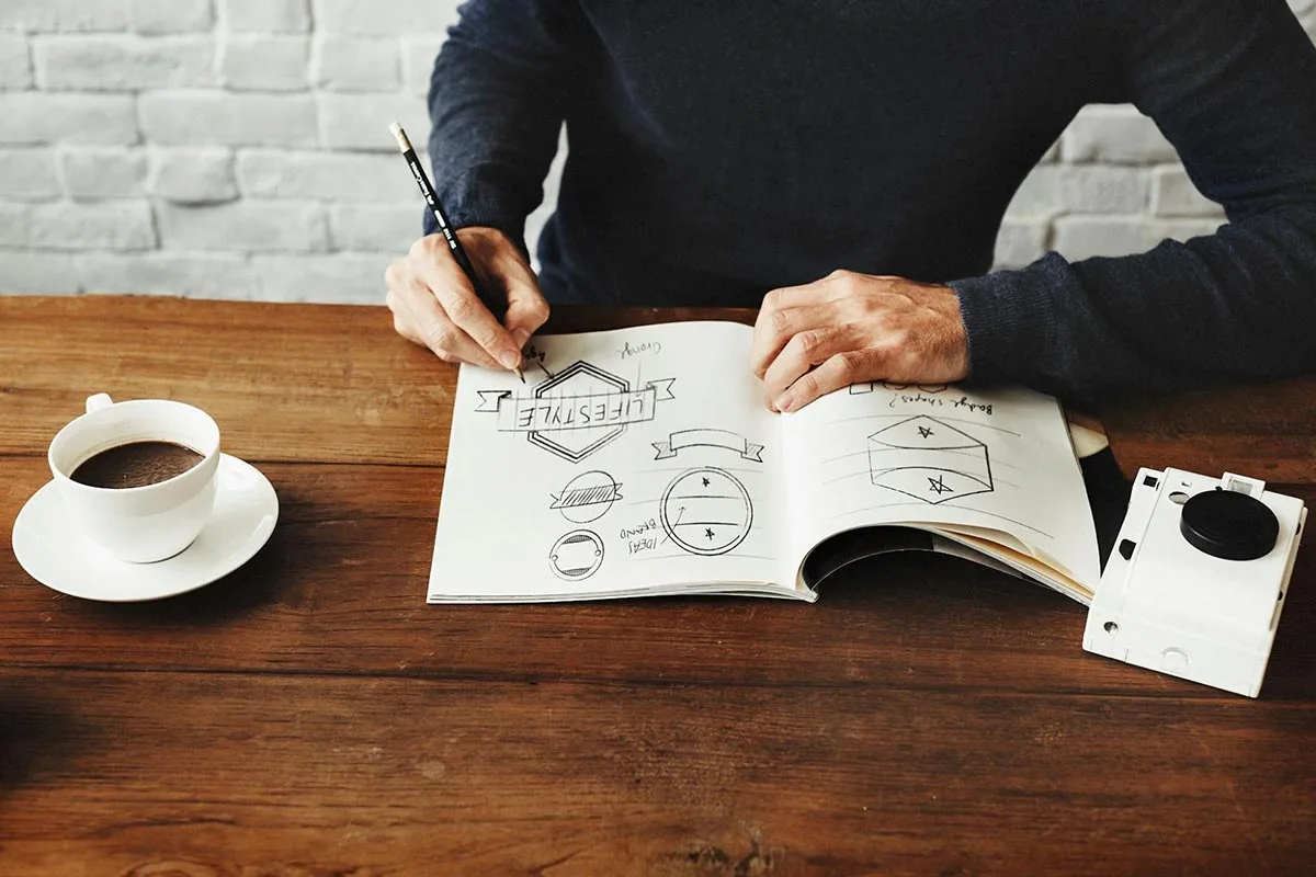 A designer sketching and mocking up logo designs on notepad.