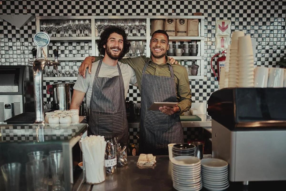 Two smiling restaurant owners posing together inside their cozy restaurant.