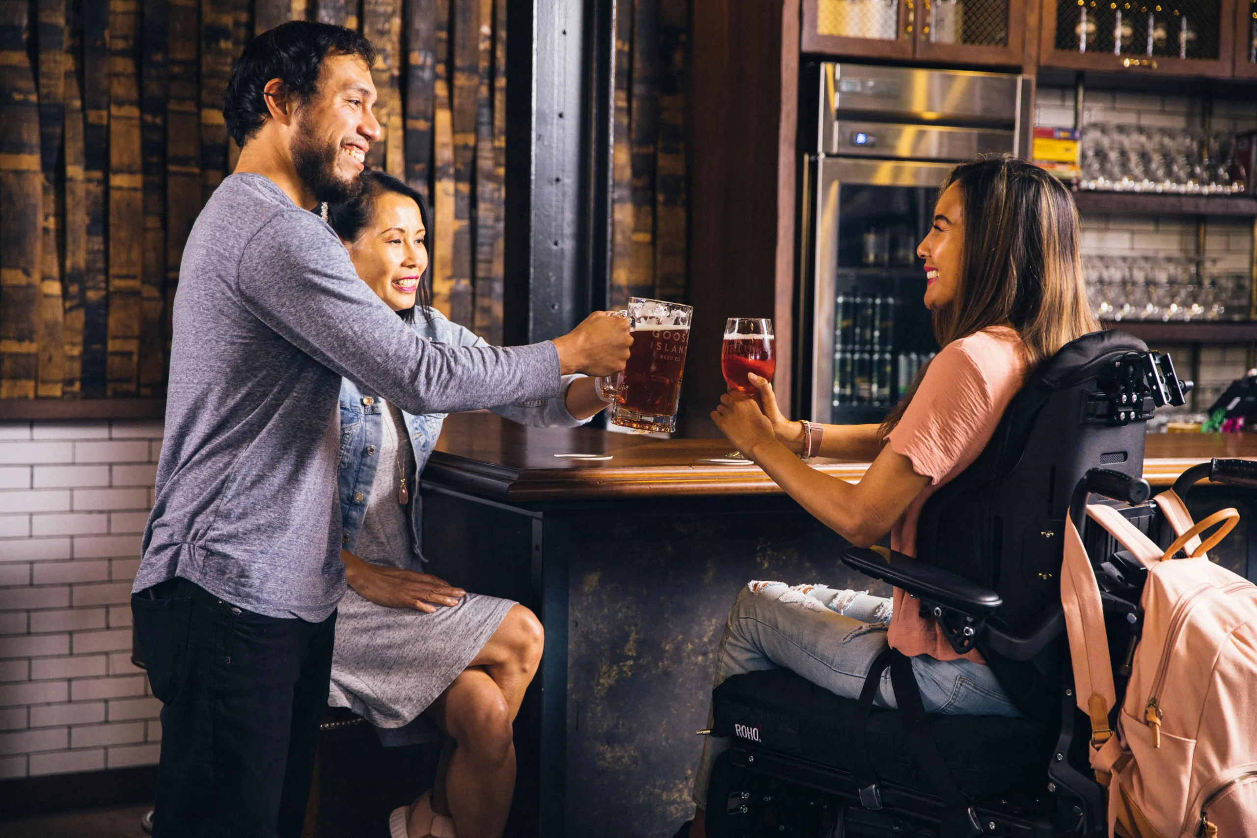 3 people toasting their beers at a bar countertop