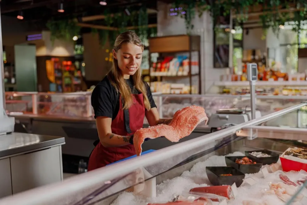 Deli owner holding a fresh salmon fillet behind the counter.