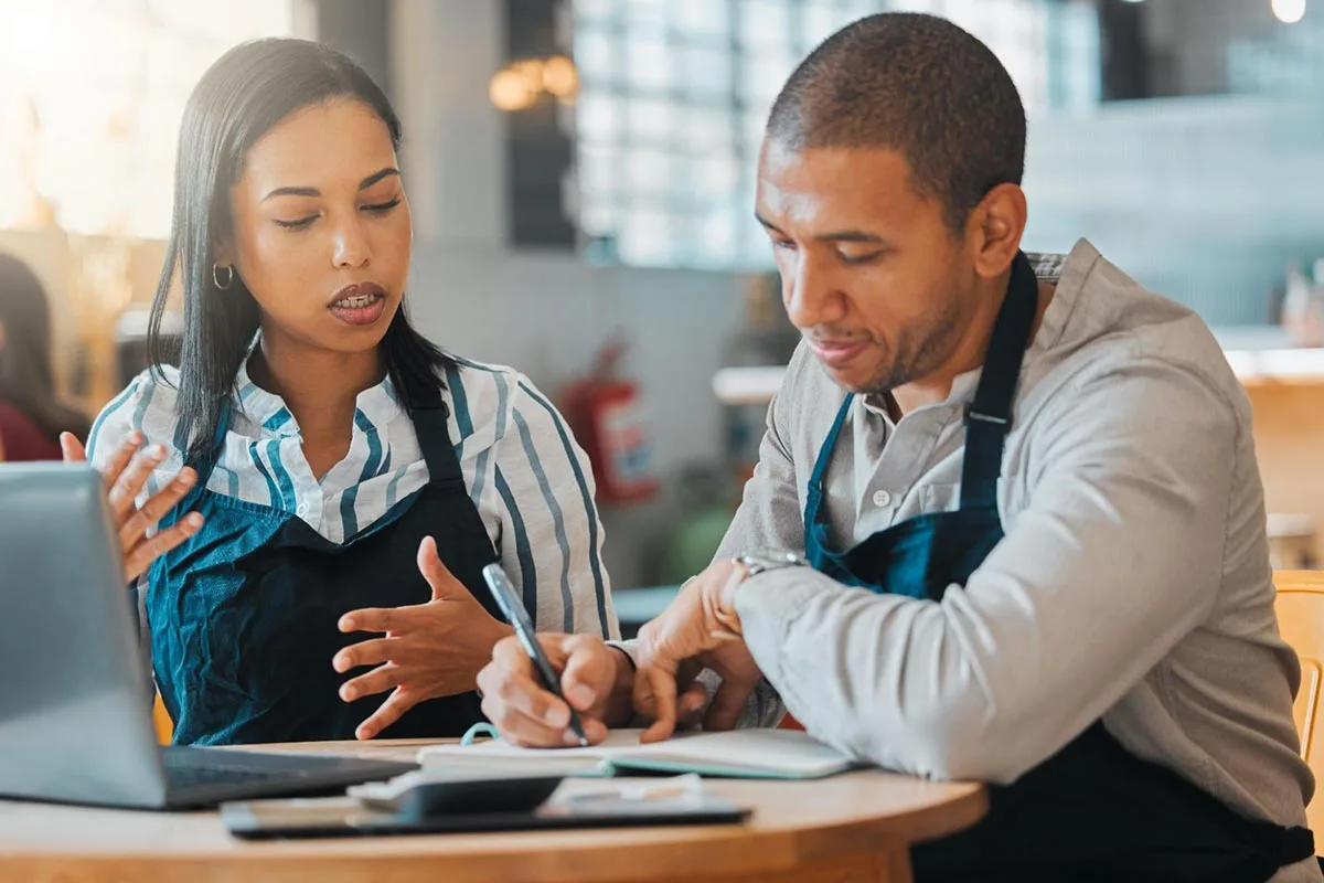 Restaurant owners reviewing analytics and customer feedback on laptop.