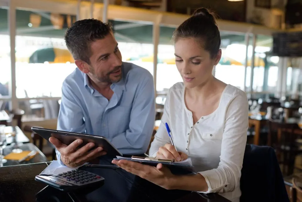 Restaurant owners in discussion while holding a tablet.