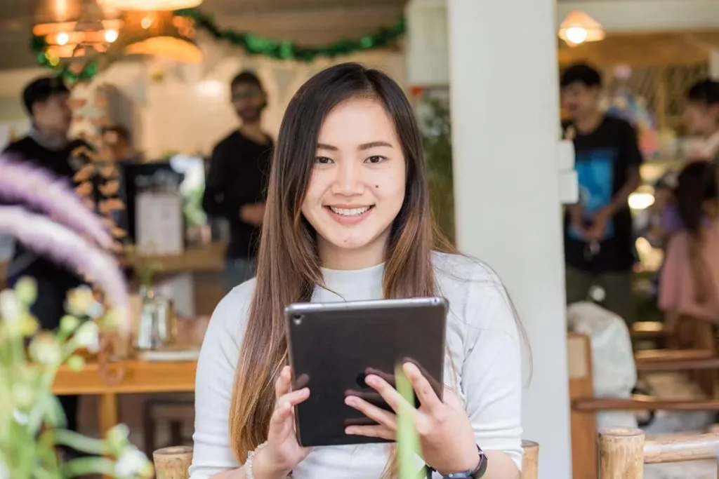 Smiling restaurant manager holding a tablet while standing in a modern restaurant.