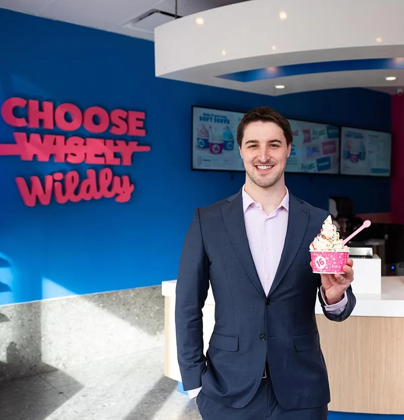 Photo of CEO Neil Hershman holding a cup of frozen yogurt inside a 16 Handles location.