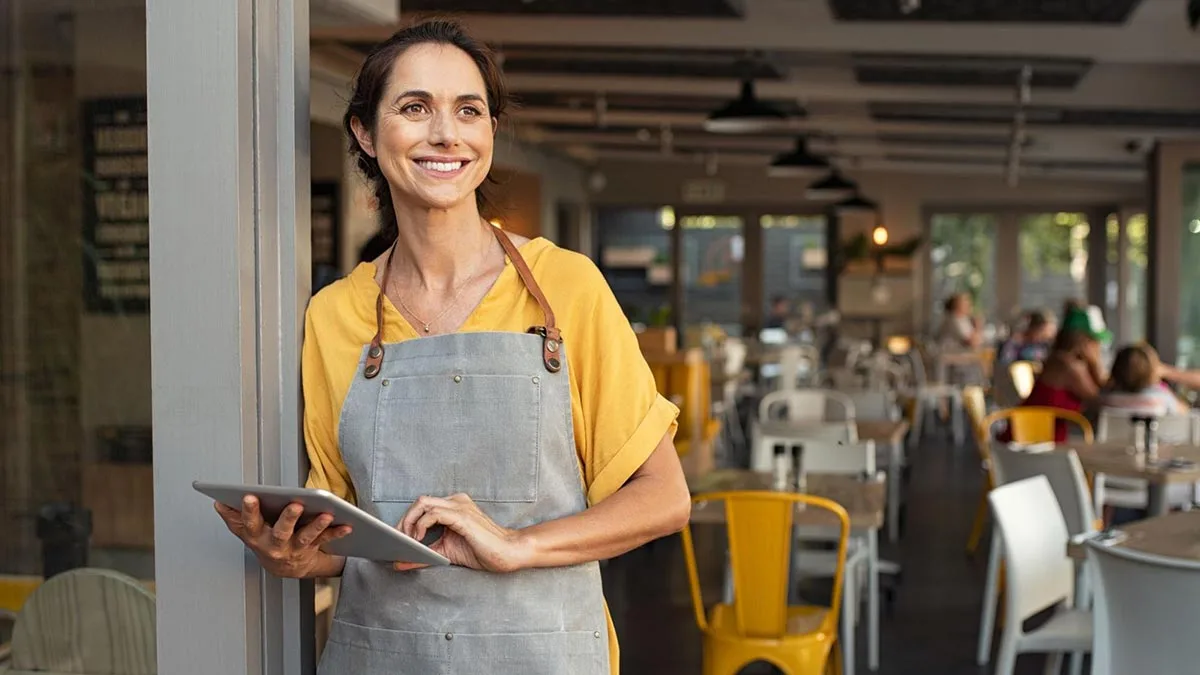 A restaurant manager is smiling while standing inside the restaurant.