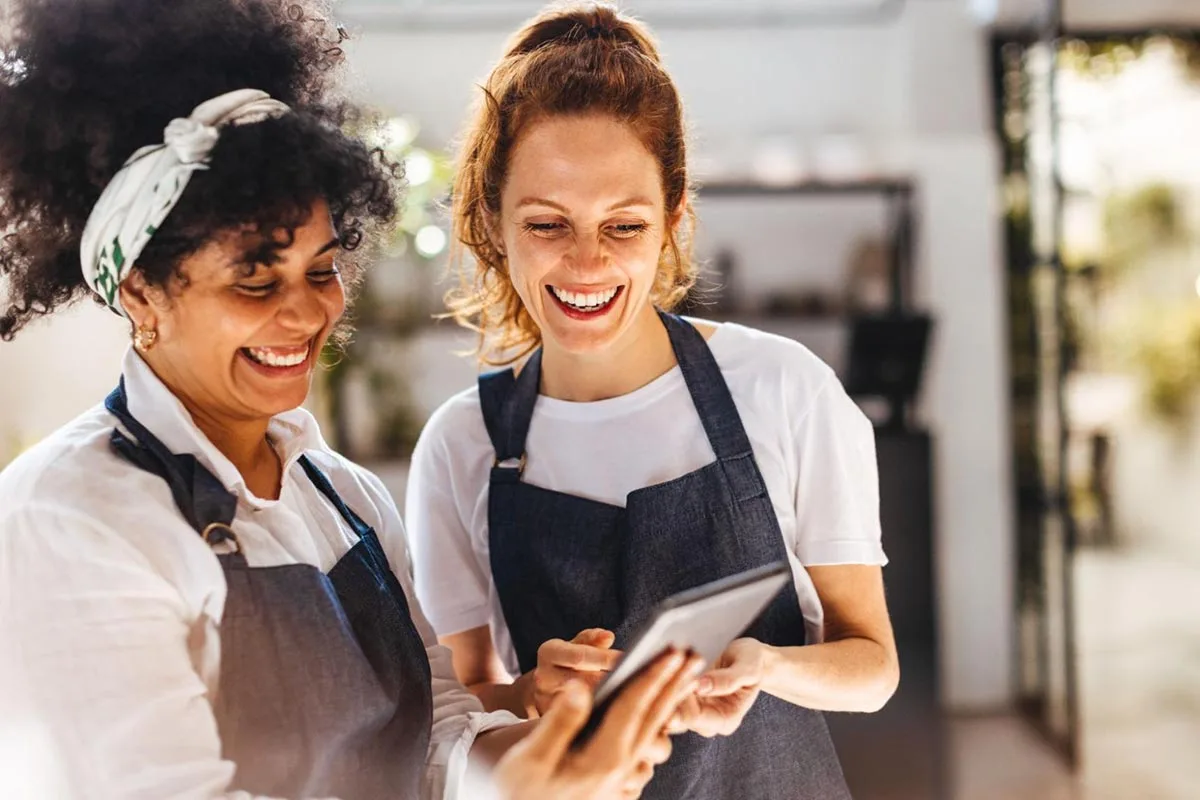 Restaurant servers are smiling as they look at a tablet to check a booking.