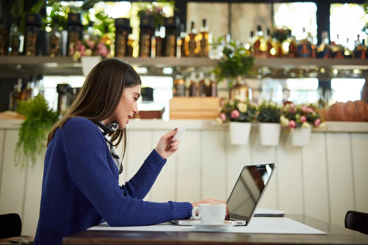 A restaurant manager sits at a table with a laptop, reviewing cost control data while enjoying a cup of coffee.