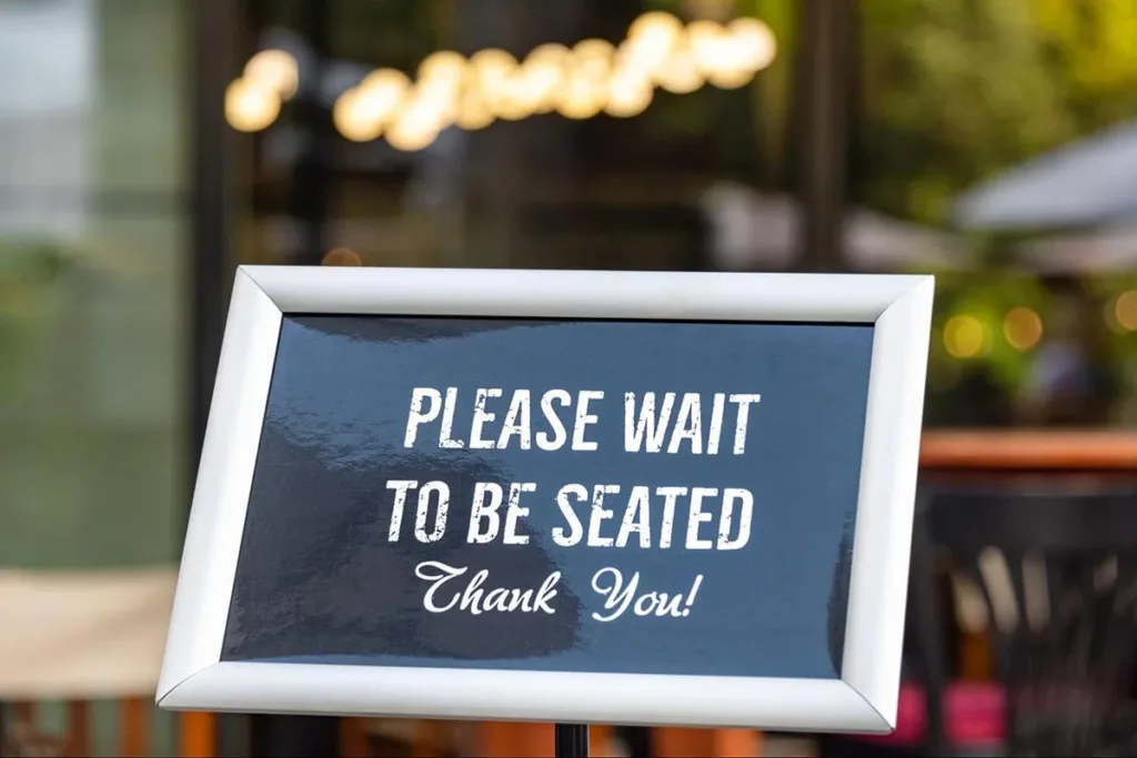 A restaurant sign that says “Please wait to be seated.”